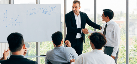 Several people in a meeting with a whiteboard, where a new employee is introduced by a business manager